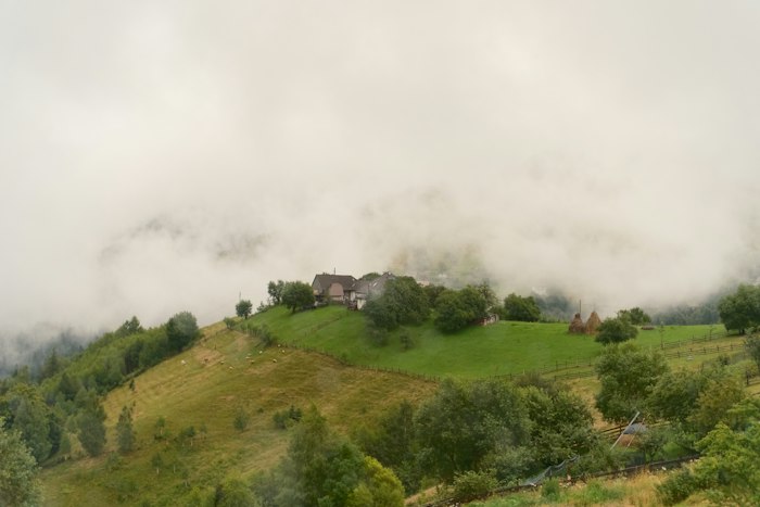 Chalé na encosta verde da serra, parcialmente coberto pela neblina